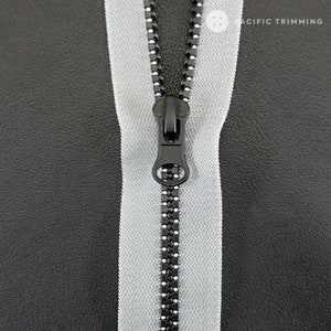 May include: A close-up of a silver zipper with a black zipper pull. The zipper is on a black fabric background.