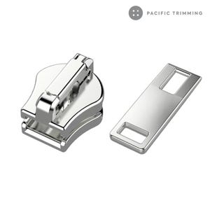 May include: A bright silver zipper slider and pull tab. The slider has a rounded base and a rectangular top section. The pull tab is a flat rectangle with a rectangular hole at each end. The text "PACIFIC TRIMMING" is visible in the upper right.