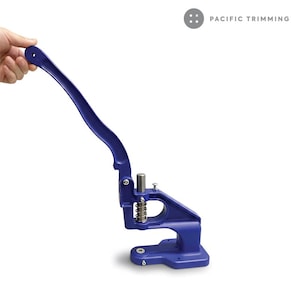 May include: A blue metal snap press tool with a long handle. The tool has a spring and a silver metal post. The text "PACIFIC TRIMMING" is visible in the upper right corner.