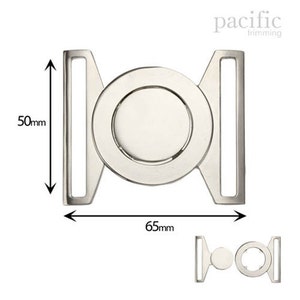 Könnte beinhalten: Silberne Metallschnalle mit rundem Mittelteil, 6,5 cm breit und 5 cm hoch. pacific trimming ist auf dem Bild aufgedruckt.