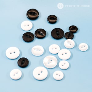 May include: Assortment of black and white plastic buttons with two holes. The buttons are scattered on a light blue background.