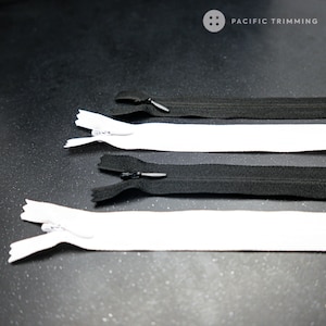 May include: Four zipper closures in two colours, black and white. The zippers are laid out in a row on a dark grey surface. The text "PACIFIC TRIMMING" is visible in the top right corner of the image.