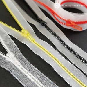 May include: Four different types of zipper tape, including clear, yellow, black, and red. The tape is laid out on a black surface. The text "PACIFIC TRIMMING" is visible in the top right corner of the image.