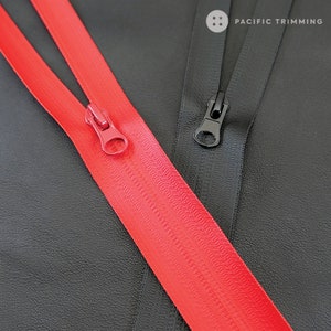 Puede incluir: Dos cintas de cremallera, una roja y otra negra, se colocan sobre una superficie negra. Los tiradores de la cremallera son visibles, uno rojo y otro negro. El texto "PACIFIC TRIMMING" es visible en la esquina superior derecha de la imagen.