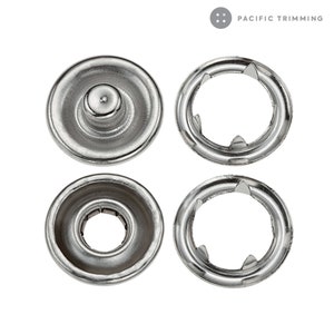 May include: Four silver metal snap fasteners, two with a raised center and two with a ring of points around the edge.