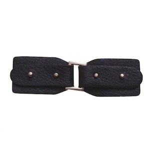 Pode incluir: Fivela de cinto de couro preto com fecho de metal prateado. A fivela tem uma superfície texturizada e é fixada com dois pequenos rebites prateados de cada lado. O design é simétrico e moderno.