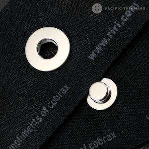 May include: Two silver metal eyelets, one with a round shape and the other with a raised center, are attached to black fabric with the text "www.riri.com" and "elements of cobrax" printed on it.