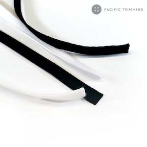 May include: Three different types of black trim, including a zipper tape, a black fabric trim, and a white fabric trim. The trim is on a white surface. The text "PACIFIC TRIMMING" is visible in the top right corner of the image.