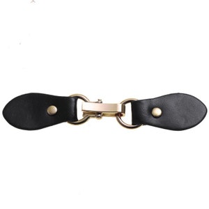 May include: A black leather toggle clasp with gold-toned metal hardware. The clasp has two leather loops and a metal bar with two rings.