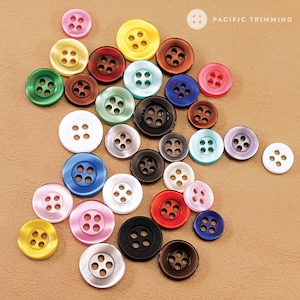 May include: Assortment of colorful plastic buttons with four holes each. The buttons are arranged in a semi-circle on a brown surface.  The buttons are in various colors, including red, blue, green, yellow, white, black, and brown.