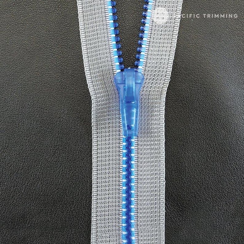 May include: A close-up of a zipper with a blue slider. The zipper tape is gray with a blue and silver thread running along the center.