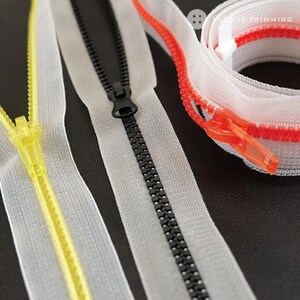 May include: Three different types of zipper tape, including black, yellow, and red, are shown on a black surface. The zipper tape is white with a contrasting color zipper.
