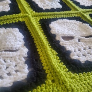 May include: A crocheted blanket with a repeating pattern of white skulls on a black background, framed by a lime green border.