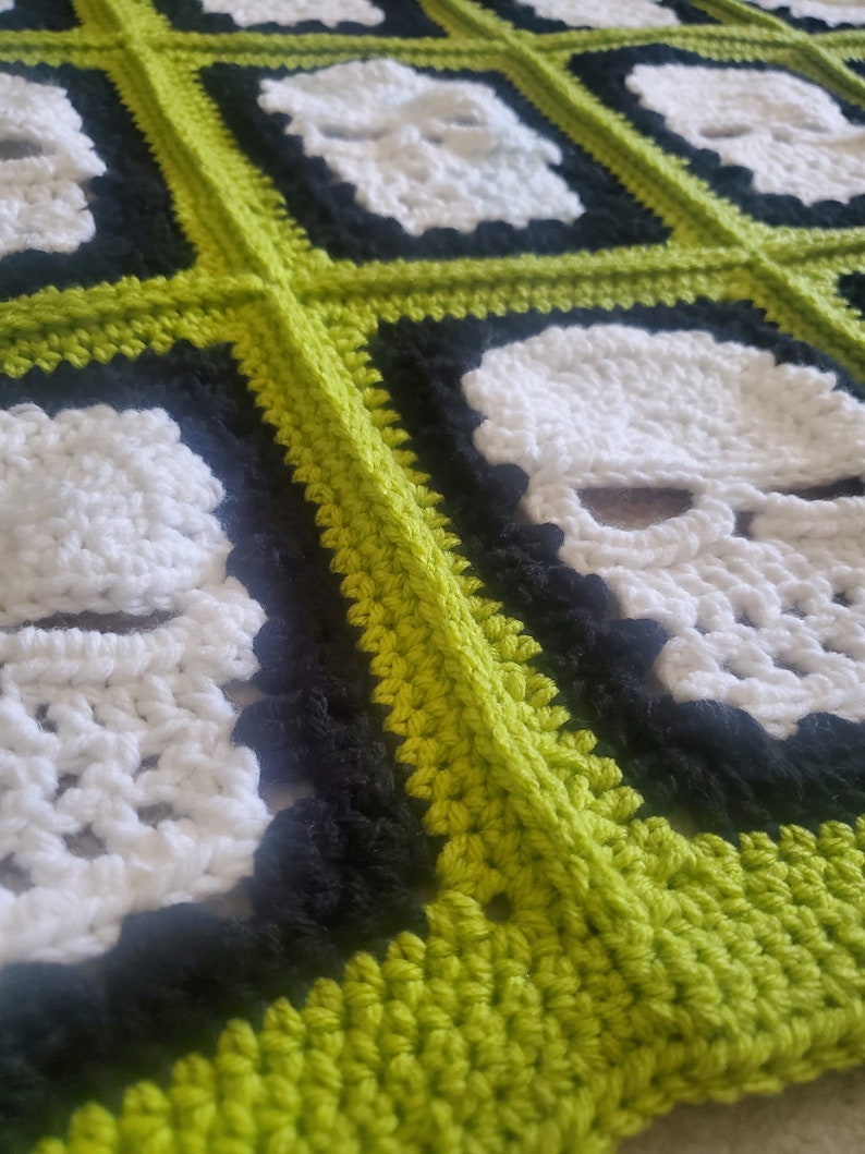 May include: A crocheted blanket with a repeating pattern of white skulls on a black background, framed by a lime green border.