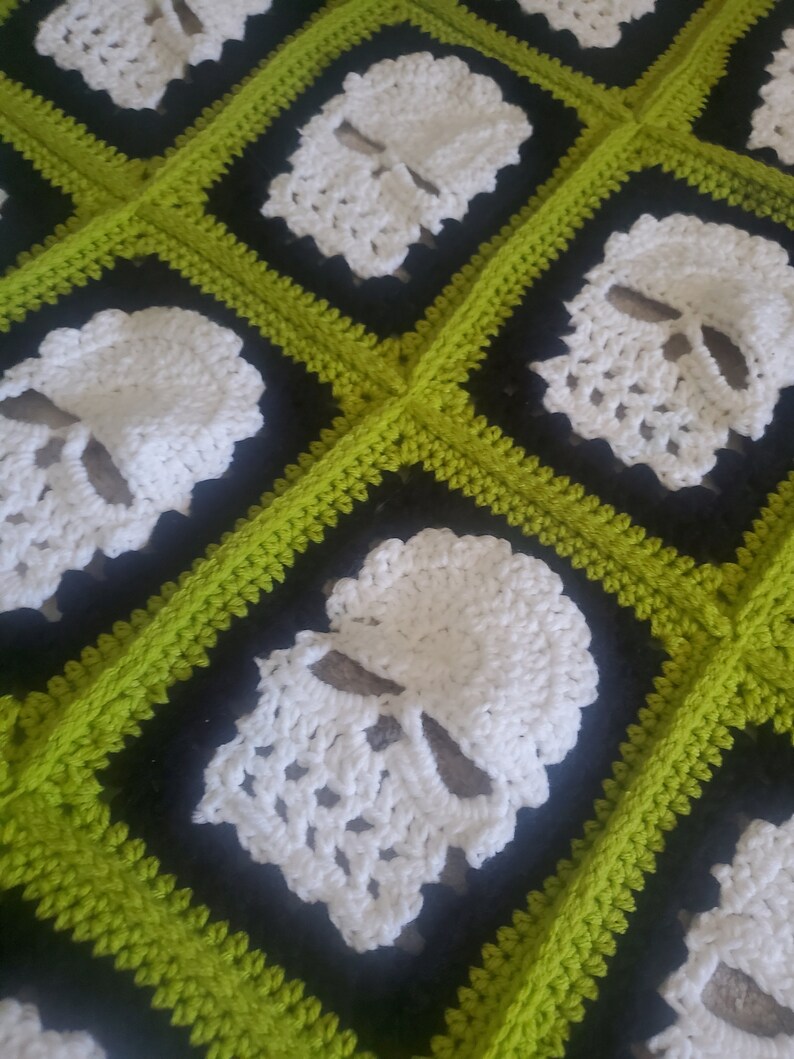 May include: A crocheted blanket with a black and green checkered pattern. Each square features a white crocheted skull design.