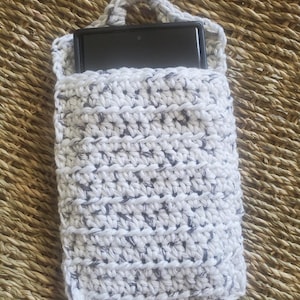 May include: A handmade crochet phone case in white with gray flecks. The case has a loop handle and holds a black smartphone. The crochet stitch creates a textured surface. The case is designed to protect and carry a phone.