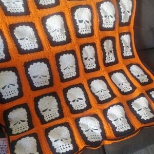 May include: A crocheted blanket with a skull pattern in white on an orange and black background.
