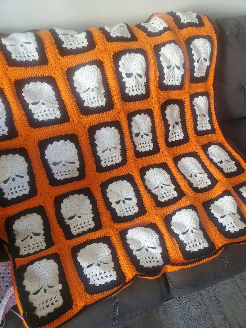 May include: A crocheted blanket with a skull pattern in white on an orange and black background.