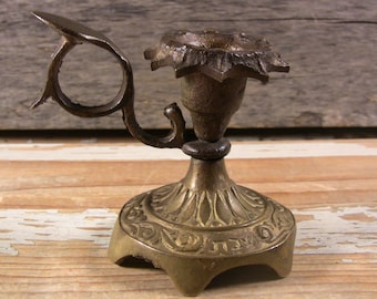 May include: A small, ornate brass candlestick with a star-shaped candle holder and a decorative base. The candlestick has a handle on the side.
