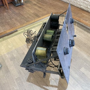 May include: A vintage radio chassis with multiple coils and knobs. The chassis is made of metal and has a black finish. The coils are wrapped in green and yellow fabric. The knobs are black plastic.