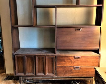 May include: A dark brown wooden wall unit with open shelves, a cabinet with doors, and two drawers. The unit has a mid-century modern style.