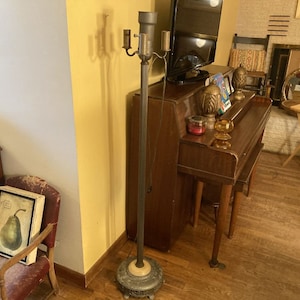 May include: A vintage floor lamp with a brass base and four lights. The lamp is standing next to a wooden piano with a decorative top.