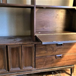 May include: A dark brown wooden cabinet with two drawers and a fold-down desk. The cabinet has a mid-century modern style and features a wood grain pattern.