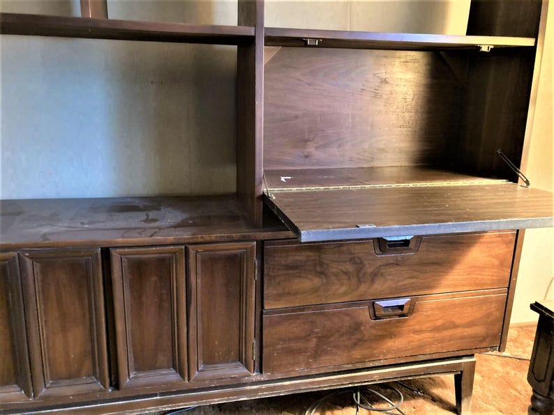 May include: A dark brown wooden cabinet with two drawers and a fold-down desk. The cabinet has a mid-century modern style and features a wood grain pattern.