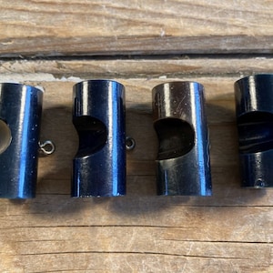 May include: Four black metal fishing sinkers with a hole in the side. The sinkers are cylindrical in shape and have a shiny finish.