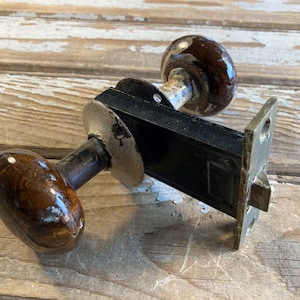 May include: A vintage door knob with a black metal plate and two brown ceramic knobs. The knobs have a marbled pattern.