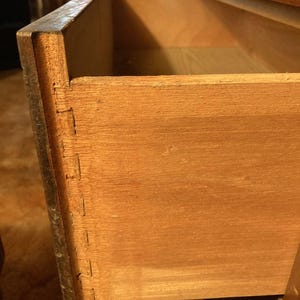 May include: Close-up of the inside of a wooden drawer. The drawer is made of light brown wood and has a dovetail joint. The drawer is open and empty.