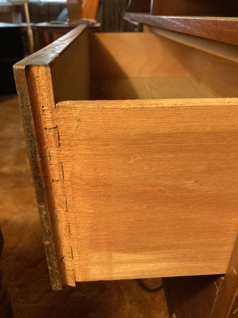 May include: Close-up of the inside of a wooden drawer. The drawer is made of light brown wood and has a dovetail joint. The drawer is open and empty.