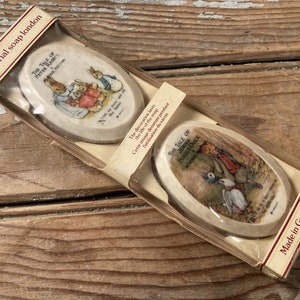 May include: Two oval-shaped soap bars featuring illustrations from the children's books "The Tale of Peter Rabbit" and "The Tale of Jemima Puddle-Duck". The soap bars are packaged in a clear plastic wrapper with a white cardboard backing. The packaging includes the text "pictorial soap london" and "Made in Great Britain".