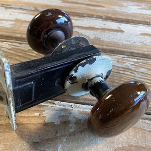 May include: A vintage door knob with a black metal base and two brown ceramic knobs. The knob has a white porcelain backplate.