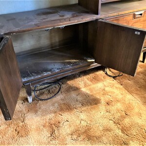 May include: A dark brown wooden cabinet with two doors and shelves. The doors are open, revealing the empty interior. The cabinet is sitting on a brown shag carpet.