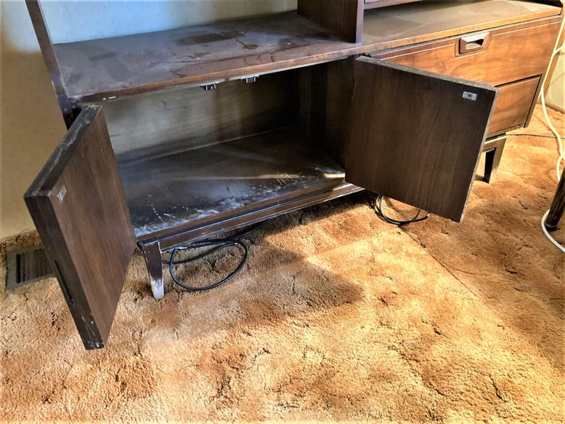 May include: A dark brown wooden cabinet with two doors and shelves. The doors are open, revealing the empty interior. The cabinet is sitting on a brown shag carpet.