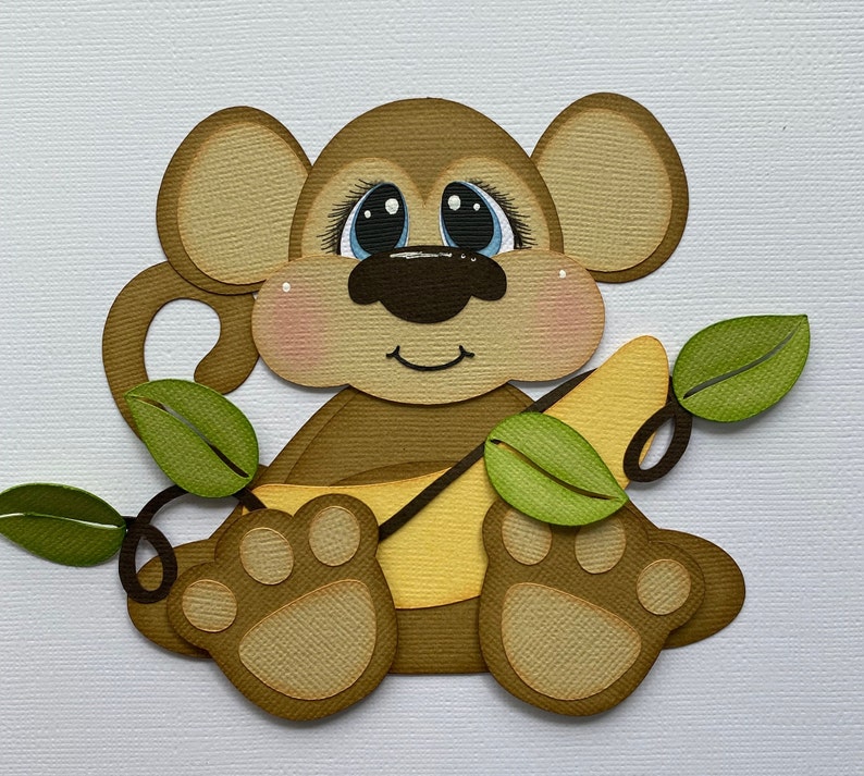 May include: A brown monkey with blue eyes holding a yellow banana. The monkey is sitting on a green vine with leaves.