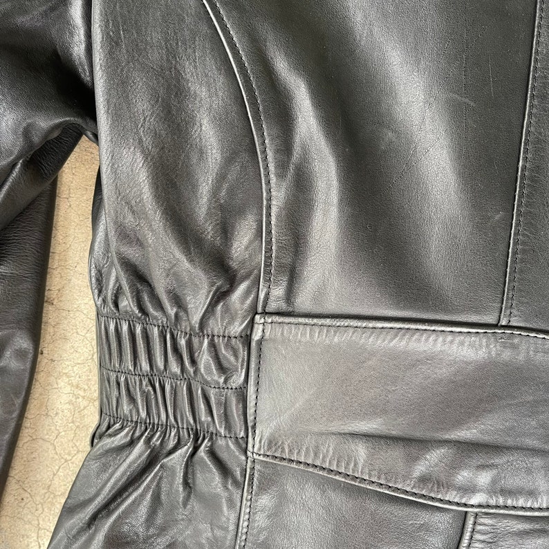 May include: Black leather jacket with a cinched waist and a zipper closure. The jacket has a smooth, textured surface.