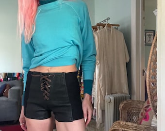 May include: A woman wearing a light blue sweatshirt and black high-waisted shorts with brown laces. The shorts have a panel of black fabric on the sides.