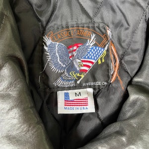 May include: A black leather jacket with a label that says "Classic Leather" and features an eagle with an American flag. The label also says "Riverside CA" and "Made in U.S.A.". The jacket is size M.