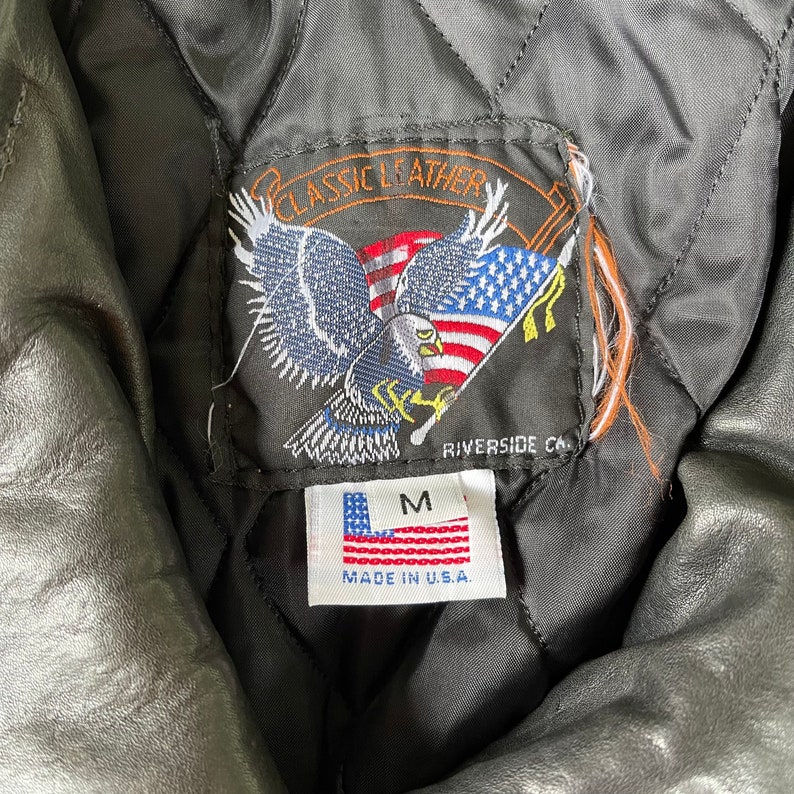May include: A black leather jacket with a label that says "Classic Leather" and features an eagle with an American flag. The label also says "Riverside CA" and "Made in U.S.A.". The jacket is size M.