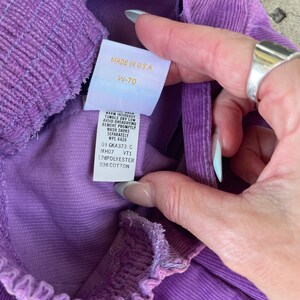 May include: Purple corduroy pants with a white tag that reads "MADE IN U.S.A. W-70" and care instructions. The tag also states "17% POLYESTER 83% COTTON".