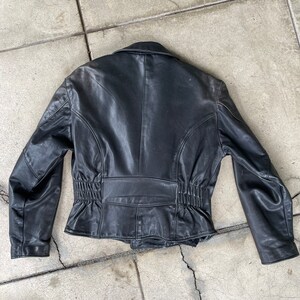 May include: Black leather jacket with a cinched waist and a zipper closure. The jacket has a collar and long sleeves.