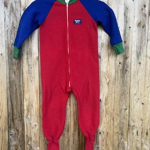 Puede incluir: Un pijama de una pieza rojo, azul y verde con cremallera completa. Las mangas y la parte superior del cuerpo son azules, con ribetes verdes alrededor del cuello y los pu&ntilde;os. Los pies son rojos con suelas blancas.