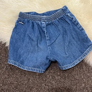 May include: Blue denim shorts with an elastic waistband. The shorts have a classic five-pocket design and are made of a durable denim fabric. The shorts are likely for a child.