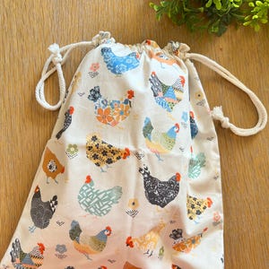 Puede incluir: Una bolsa de algod&oacute;n blanco con cord&oacute;n de ajuste y un estampado de pollos coloridos. La bolsa tiene un cord&oacute;n de ajuste blanco y es perfecta para llevar objetos peque&ntilde;os.