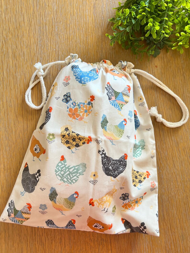 Puede incluir: Una bolsa de algod&oacute;n blanco con cord&oacute;n de ajuste y un estampado de pollos coloridos. La bolsa tiene un cord&oacute;n de ajuste blanco y es perfecta para llevar objetos peque&ntilde;os.