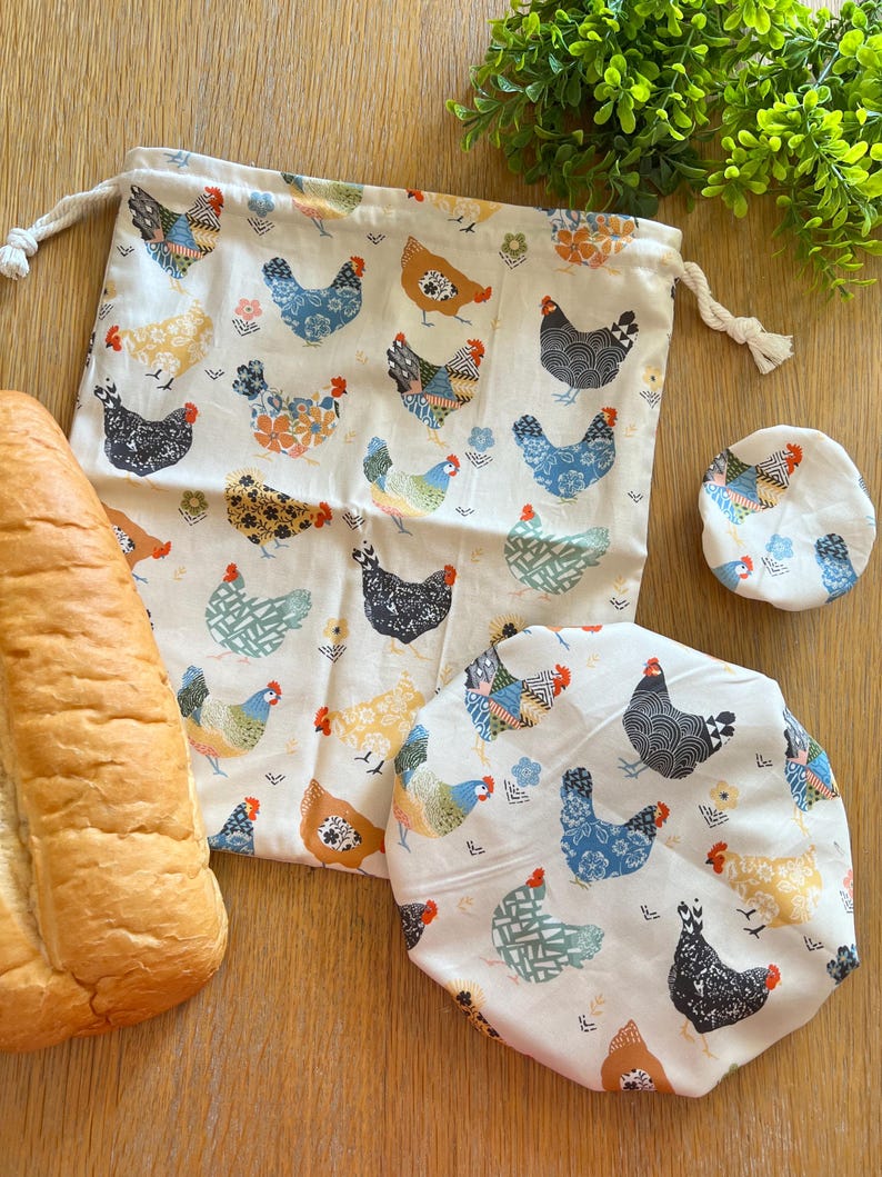 Puede incluir: Un juego de tres bolsas de almacenamiento de alimentos reutilizables con fondo blanco y un patr&oacute;n de pollo colorido. Las bolsas est&aacute;n hechas de algod&oacute;n y tienen un cierre de cord&oacute;n. Las bolsas son perfectas para guardar alimentos en el refrigerador o congelador.