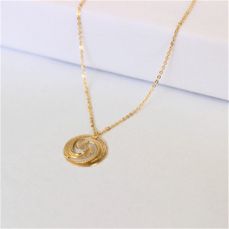 May include: A gold chain necklace with a circular pendant featuring a swirling, textured design.