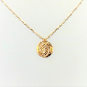 May include: A gold necklace with a circular pendant featuring a stylized wave design.